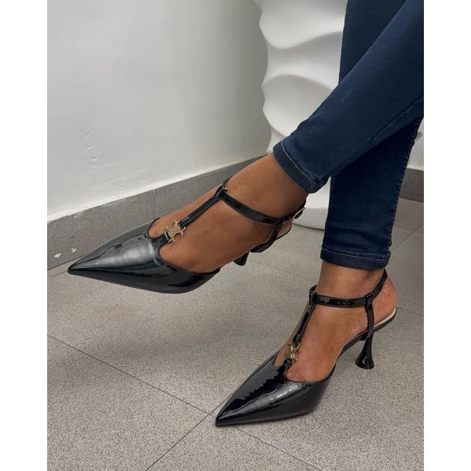 Black patent leather high heels worn with blue jeans on a neutral background