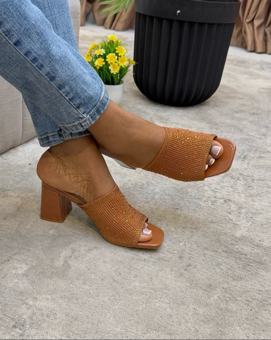 Brown open-toe heeled sandals worn with blue jeans on a concrete floor.