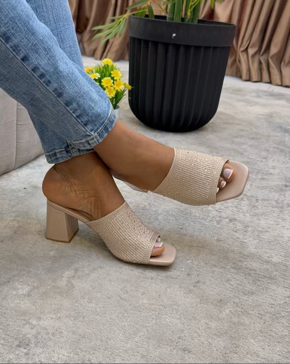 Beige open-toe heeled sandals worn with blue jeans on a light gray floor.