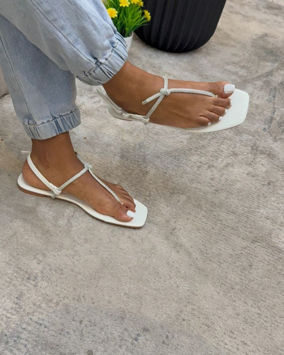 White sandals worn on a concrete surface with a person wearing light blue jeans.