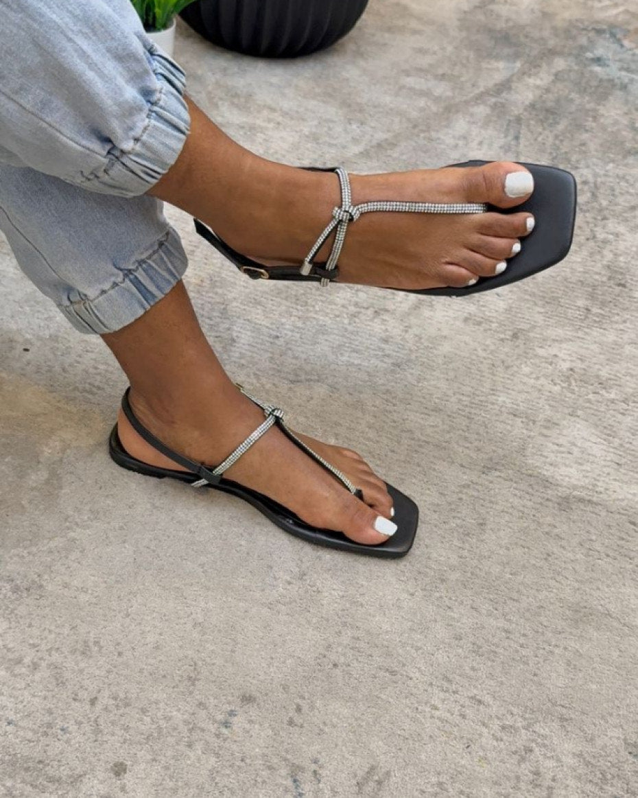 Black sandals with thin straps worn on a concrete surface